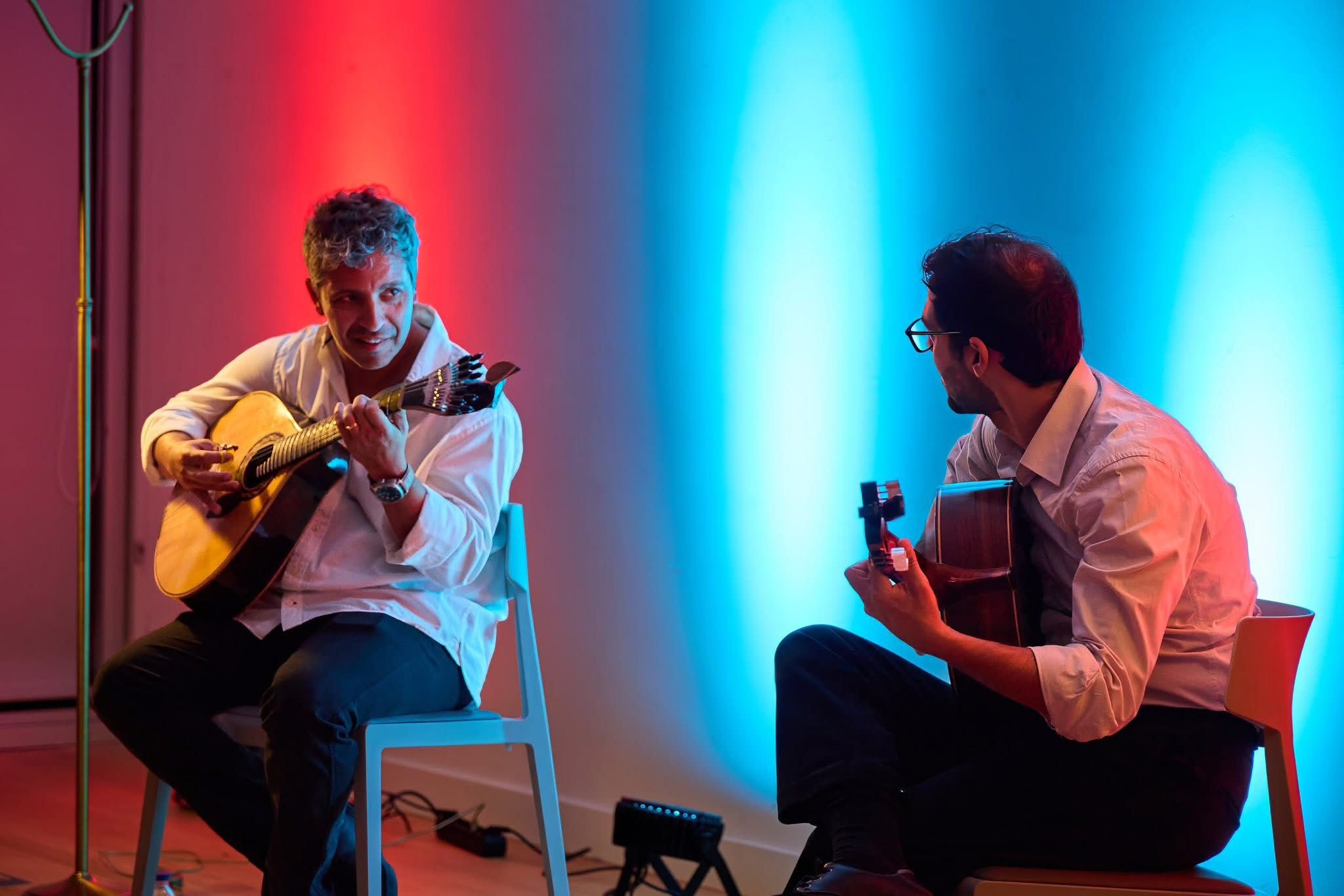 Dois guitarristas em diálogo instrumental sob iluminação vermelha e azul