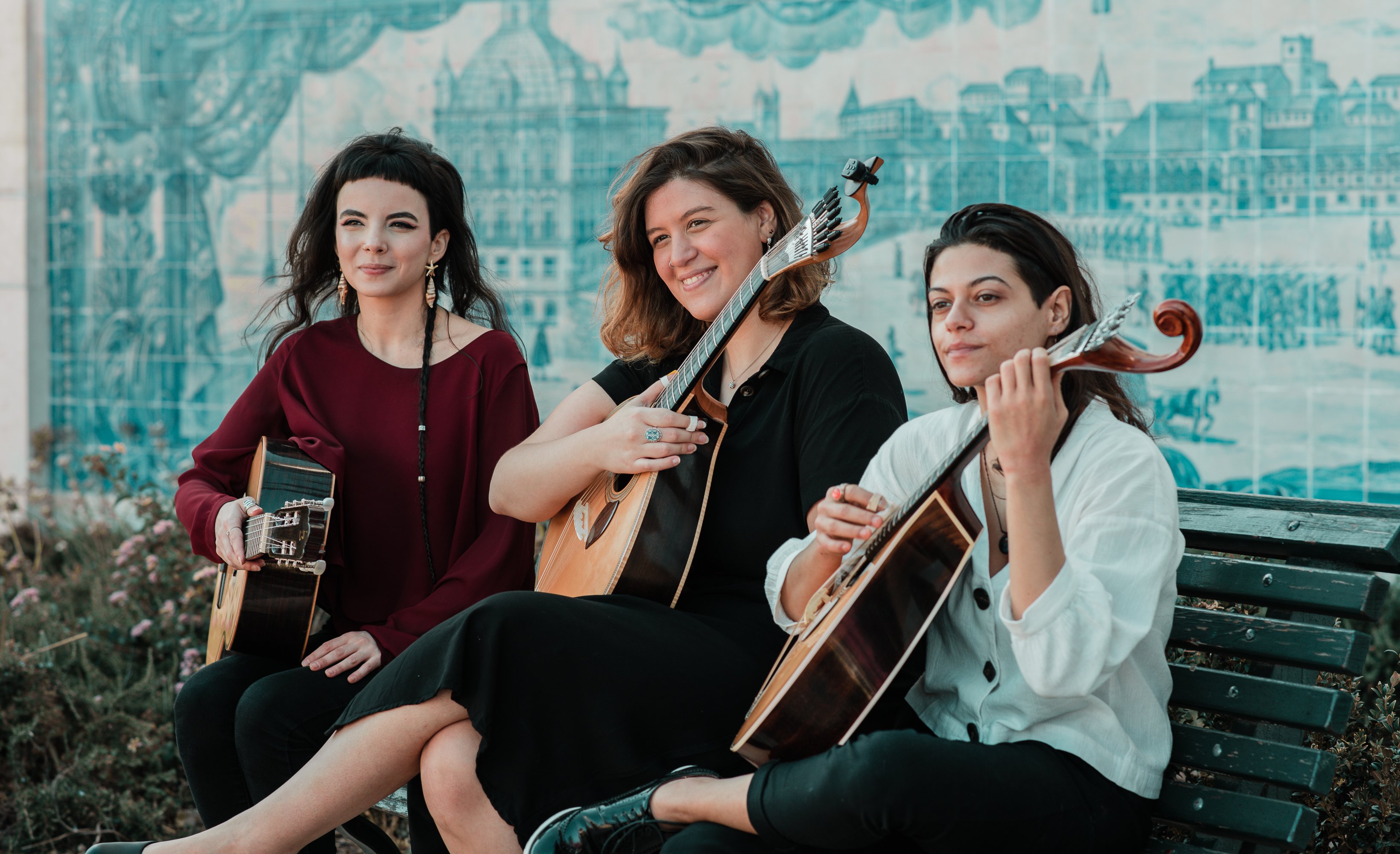 Três músicas sentadas num banco com guitarras portuguesas e viola, com painel de azulejos azuis ao fundo